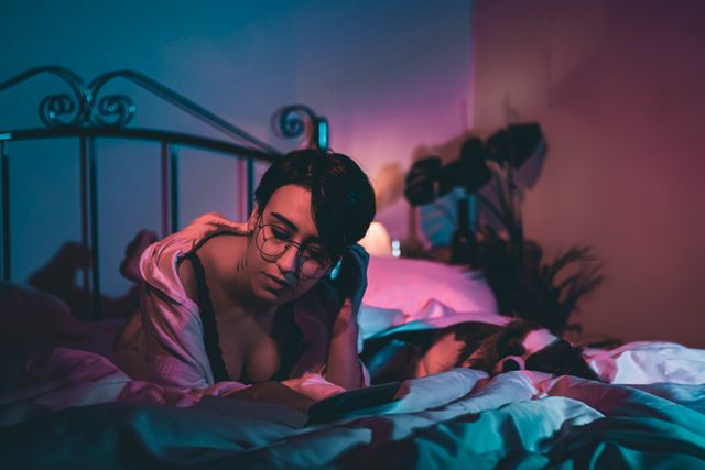 A woman with glasses experiences anxiety at night, in a dimly lit bedroom setting.