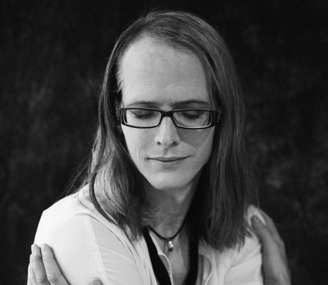 Monochrome portrait of a transgender individual with eyeglasses embracing themselves. Captured in a classic style.