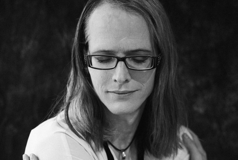 Monochrome portrait of an individual with eyeglasses embracing themselves. Captured in a classic style.