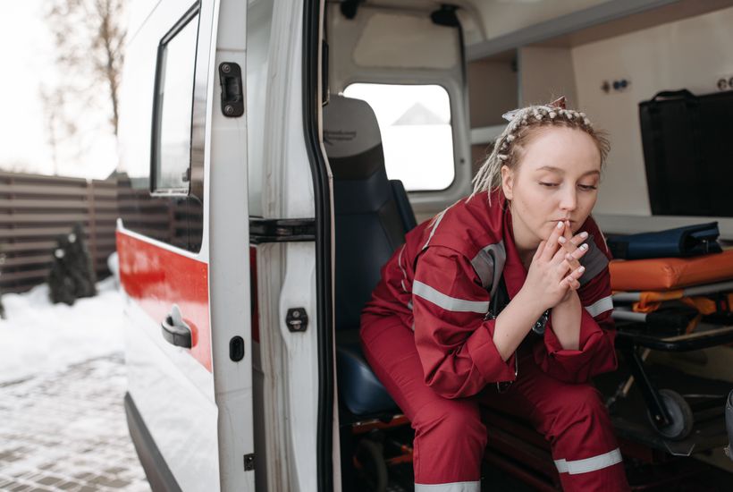 A female first responder sits pensively beside an ambulance, reflecting on duty.